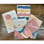 Four sympathy greeting cards with pastel abstract designs on a wooden surface