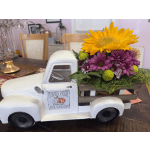 Flower arrangement in a white pickup truck planter with a sunflower and purple daisies