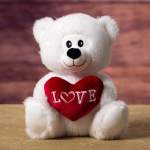 White teddy bear holding a red heart with the word LOVE