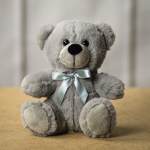 Gray teddy bear with a silver ribbon sitting on a surface