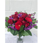 Bouquet of red roses, gerbera daisies, and purple flowers in a glass vase