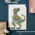 Framed dinosaur illustration on a desk with stationery and a small flower card