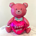 Pink teddy bear balloon holding a heart balloon that says Love you