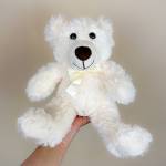 White teddy bear with a ribbon bow being held in one hand