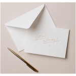 White envelope and card with gold script beside a gold pen