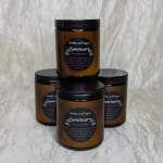 Four amber jar candles with black lids stacked on a light fabric background