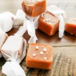 Orange square candies wrapped in white paper on a wooden surface