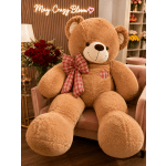 Large teddy bear with a plaid bow sitting beside a bouquet of red roses