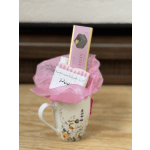 A mug gift set wrapped in pink tissue with a candy bar and packaged treat.