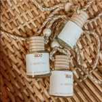 Three small gardenia car diffuser bottles with rope cords on a woven mat.