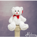 White teddy bear with a red bow sitting on a decorative pedestal