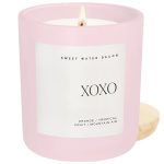 Pink scented candle in a glass jar with a lit wick