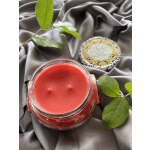 Red candle in a glass jar with a decorative lid and green leaves