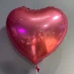 Pink heart-shaped foil balloon against a wall