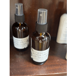 Two amber room spray bottles with clear caps sit on a wooden shelf.