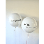 Two clear balloons with black lettering and pink ribbons on a wall