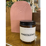 Honeysuckle soy wax candle in an amber jar with a pink decorative object behind it
