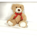 Tan teddy bear with a red ribbon sitting on a white surface