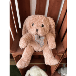 Pink plush teddy bear with a plaid bow sitting on a wooden shelf
