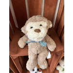 Plush teddy bear with a blue plaid bow sitting on a wooden shelf