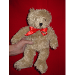 A beige teddy bear with a red ribbon bow is held against a red background.