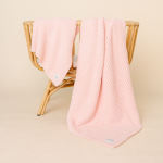 A pale pink textured blanket draped over a wicker chair