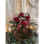 Red and pink rose arrangement in a glass vase with candles and draped fabric
