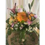Mixed bouquet with orange gerbera, pink roses, daisies, and a butterfly decoration in a glass vase
