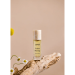 Perfume bottle on a piece of driftwood with small daisies nearby