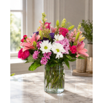 Mixed bouquet of pink lilies, roses, daisies, and purple blooms in a glass vase