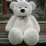 Large white teddy bear with a plaid bow sitting outdoors