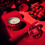 Red candle tin and cherry gloss compact on a red surface with cherries