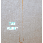 A thin gold necklace laid flat on a light fabric background.