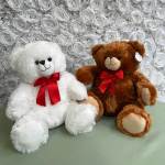 Two plush teddy bears with red bows in front of a white rose wall