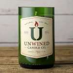 Green glass jar candle with cream label reading Unwined Candle Co. on a wooden surface
