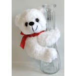 White teddy bear hugging a clear glass vase with a red ribbon