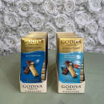 Two Godiva chocolate gift boxes on a table in front of a white rose backdrop