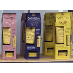 Boxes of Naked Bee hand lotion and body butter in pink, purple, and yellow packaging