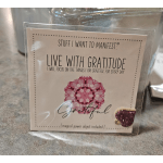 A packaged gratitude card with a pink mandala design and glitter heart charm