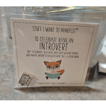 A packaged card with an illustrated fox reading a book and a small metal charm.