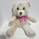 Plush teddy bear with a pink bow sitting on a white surface