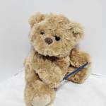 Small tan teddy bear plush toy sitting on a white surface