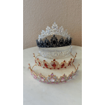 Four jeweled tiaras in silver, black, red, and pink sit stacked on a table.