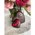 Pink flowers in a glass vase with two heart-shaped chocolates in front