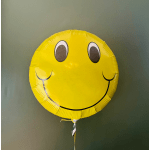 Yellow smiley face balloon against a plain wall