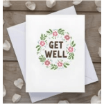 White get well greeting card with floral wreath design and matching white envelope underneath.