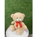 Beige teddy bear with a red bow sitting on a round white stool