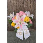 Bouquet of pink lilies and yellow and pink roses with a white Class of 2026 ribbon.