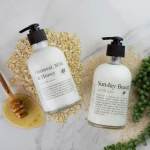 Two lotion bottles with a honey dipper and oats on a marble surface.
