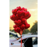 Cluster of red heart-shaped balloons held beside a car